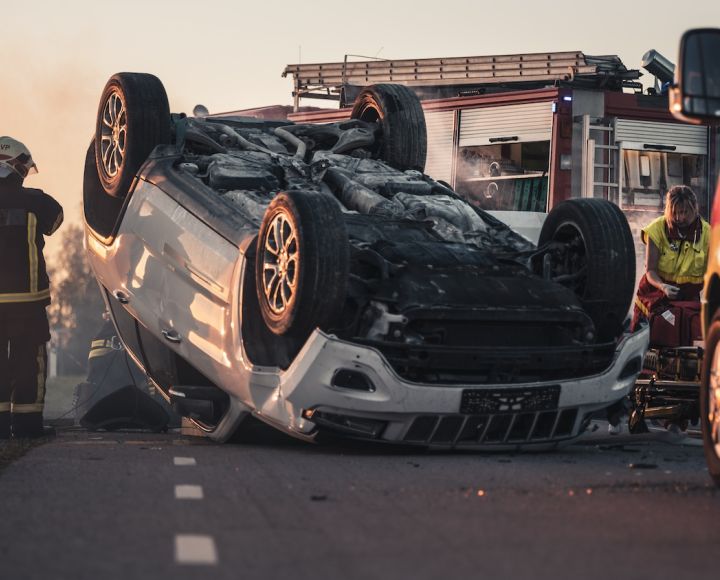 Horrific Traffic Accident Rollover Smoking and Burning Vehicle Lying on its Roof in the Middle of the Road after Collision Daytime Crash Scene with Damaged Car